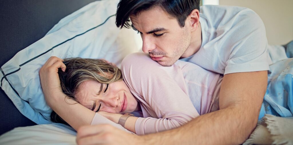 Ein Mann, der versucht, seine auf dem Bett liegende, weindende Partnerin zu beruhigen