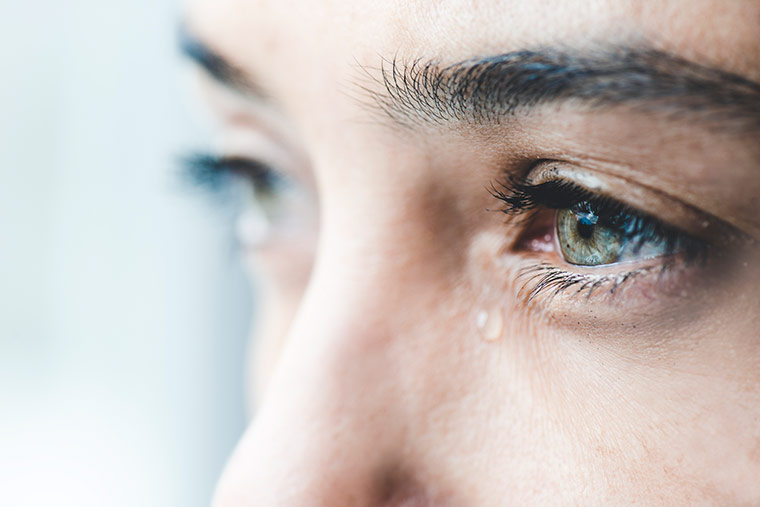 Eine Frau mit blauen Augen und einer Träne. Das Foto zeigt lediglich die Augen und einen Teil der Nase.