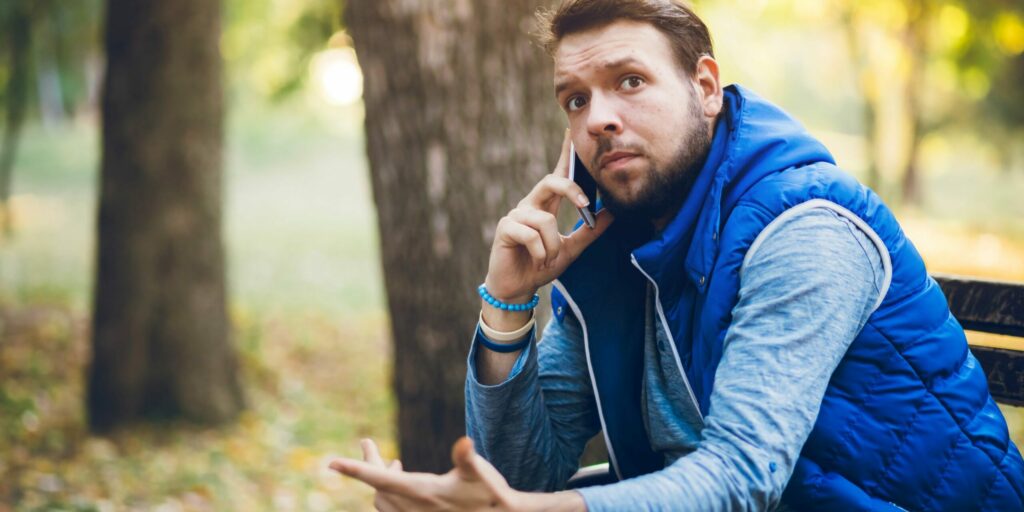 Junger Mann benutzt Mobiltelefon in einem öffentlichen Park