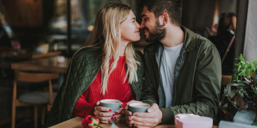 Romantisches Date. Charmantes Mädchen und ihr Freund sitzen am Tisch und halten Tassen Kaffee in der Hand