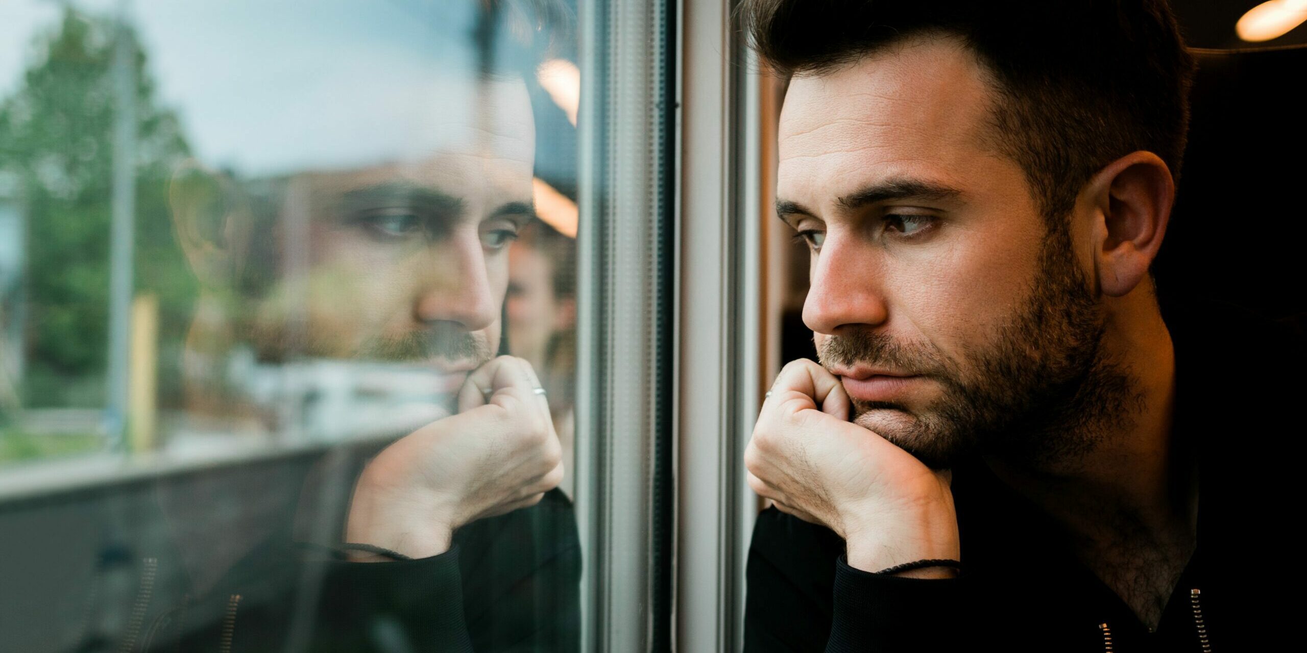 Junger bärtiger Mann reist am späten Nachmittag mit dem Zug und schaut verträumt aus dem Fenster