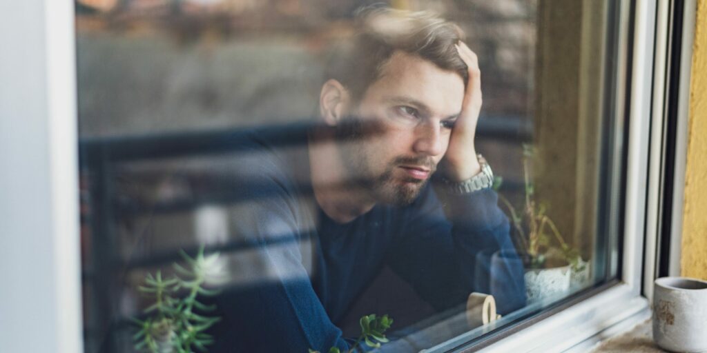 Junger Mann in Depression. Porträt von ihm durch ein Fenster.