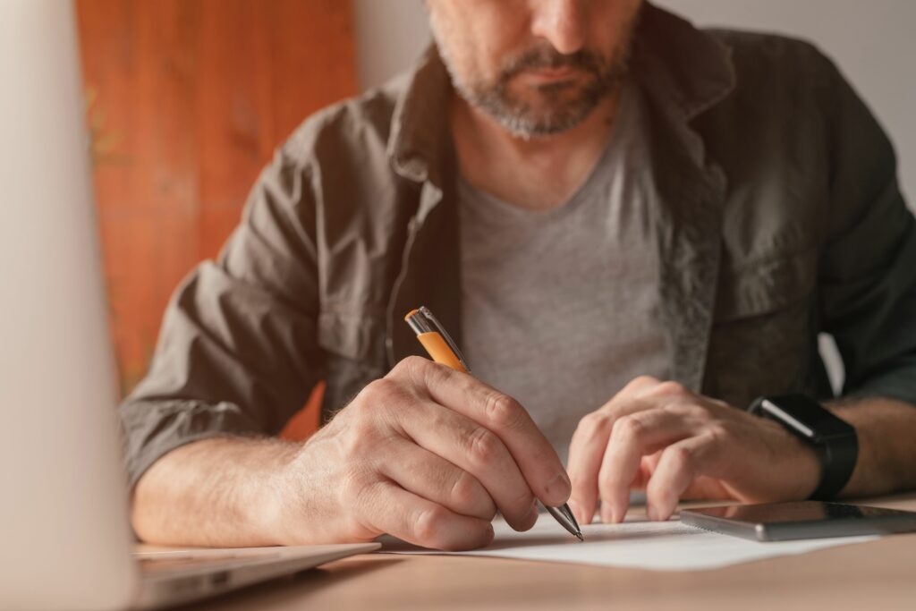 Mann schreibt am heimischen Schreibtisch Notizen auf Papier, Nahaufnahme mit selektivem Fokus