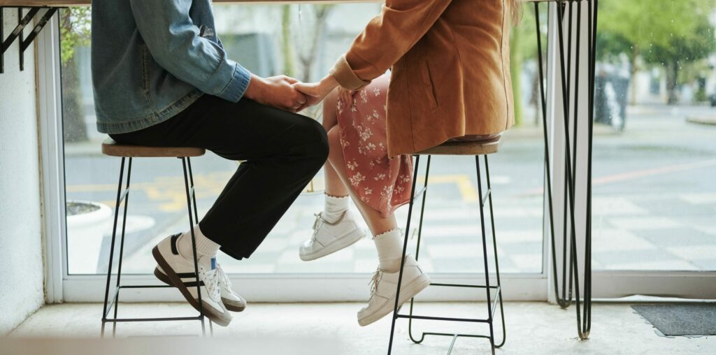 Unerkennbares junges Paar hält Händchen, während es während eines Dates zusammen am Fenster in einem Café sitzt