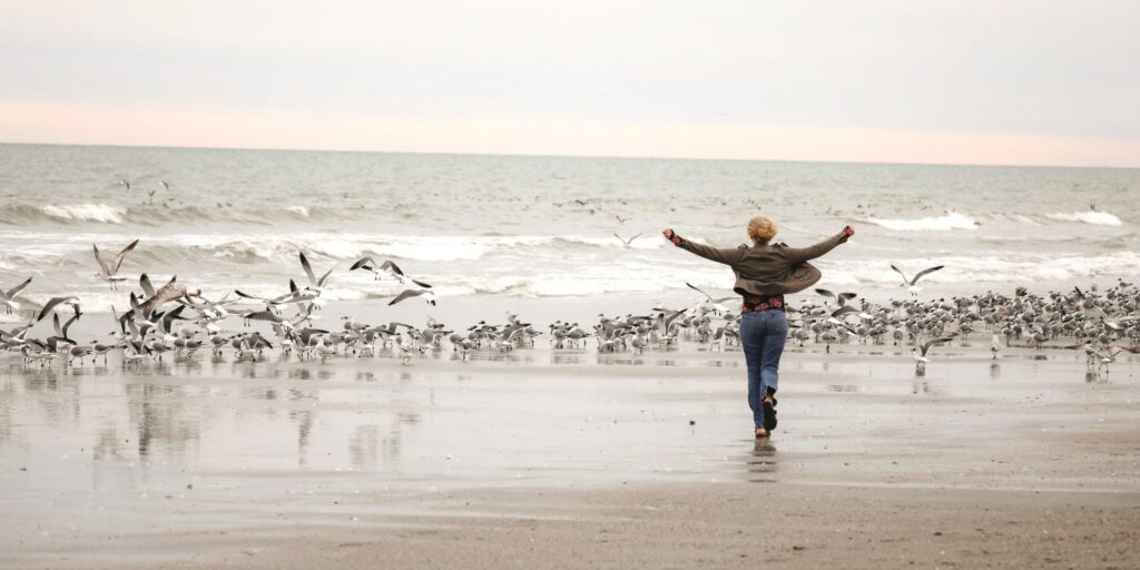 Eine Frau rennt auf Möwen am Meer zu.